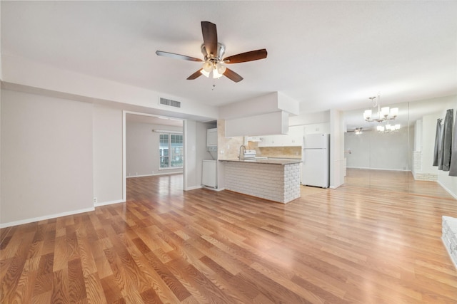 unfurnished living room with sink, ceiling fan with notable chandelier, and light wood-type flooring