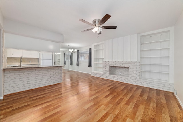 unfurnished living room featuring ceiling fan with notable chandelier, built in shelves, sink, and light wood-type flooring