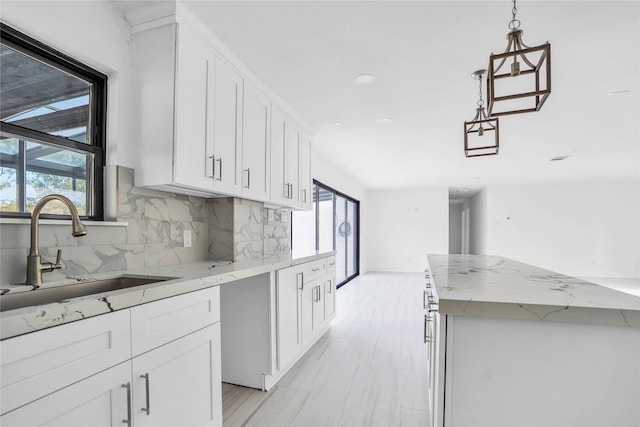 kitchen featuring white cabinetry, sink, light stone counters, and backsplash