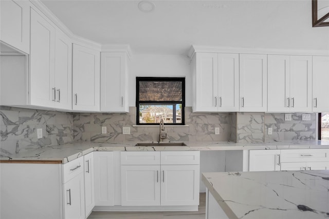 kitchen with white cabinetry, sink, light stone counters, and backsplash