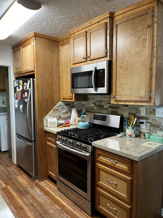 kitchen featuring washer / dryer, appliances with stainless steel finishes, light stone countertops, light hardwood / wood-style floors, and decorative backsplash