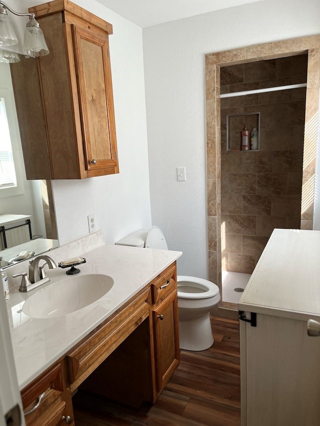 bathroom with hardwood / wood-style flooring, vanity, a tile shower, and toilet