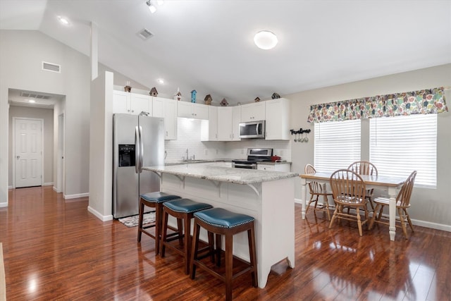 kitchen featuring lofted ceiling, white cabinetry, light stone counters, a kitchen breakfast bar, and stainless steel appliances