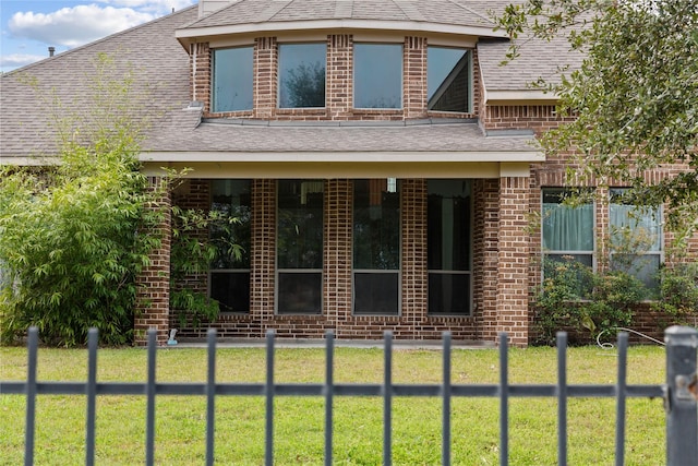 view of front facade with brick siding, a front lawn, and roof with shingles