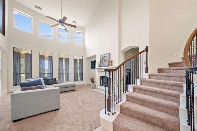 carpeted living room featuring ceiling fan, stairway, a fireplace with flush hearth, and visible vents