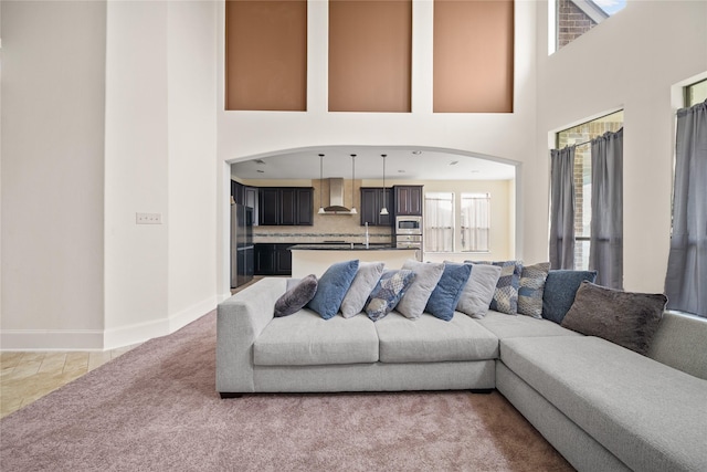 living room featuring light colored carpet, a towering ceiling, and baseboards