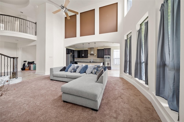 living area featuring light carpet, stairs, baseboards, and a ceiling fan