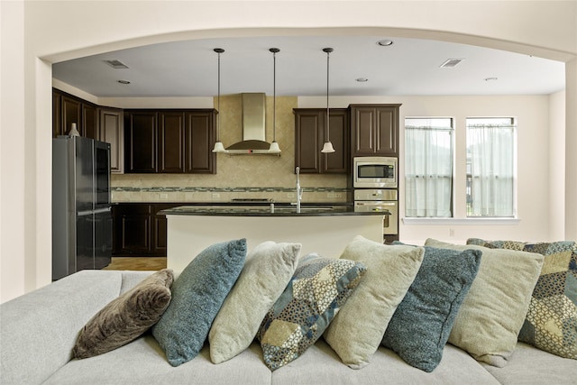 kitchen featuring open floor plan, wall chimney exhaust hood, dark brown cabinetry, and stainless steel appliances