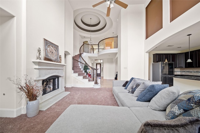 living room featuring a fireplace with raised hearth, a high ceiling, baseboards, stairs, and carpet