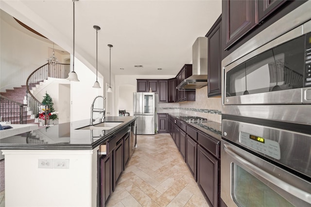 kitchen featuring a sink, appliances with stainless steel finishes, wall chimney range hood, tasteful backsplash, and dark countertops