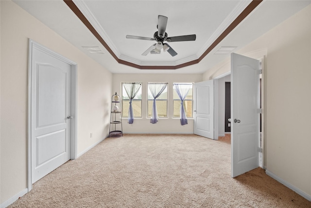 empty room featuring ornamental molding, a raised ceiling, light colored carpet, and baseboards