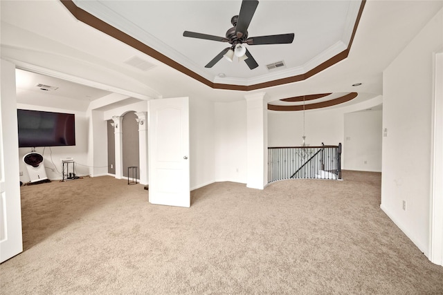 carpeted empty room with a tray ceiling, crown molding, visible vents, ceiling fan, and ornate columns