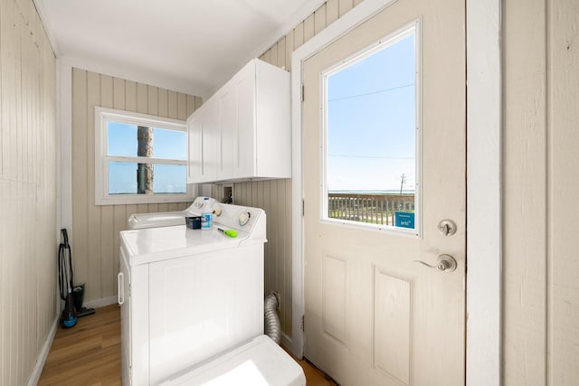 laundry room with cabinets, wooden walls, washing machine and dryer, and light wood-type flooring