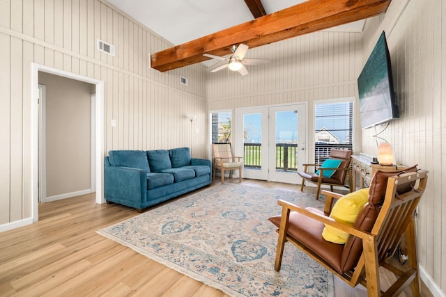 living room featuring ceiling fan, light wood-type flooring, wooden walls, and beam ceiling