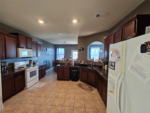 kitchen featuring light tile patterned flooring, sink, dark stone counters, dark brown cabinets, and white appliances