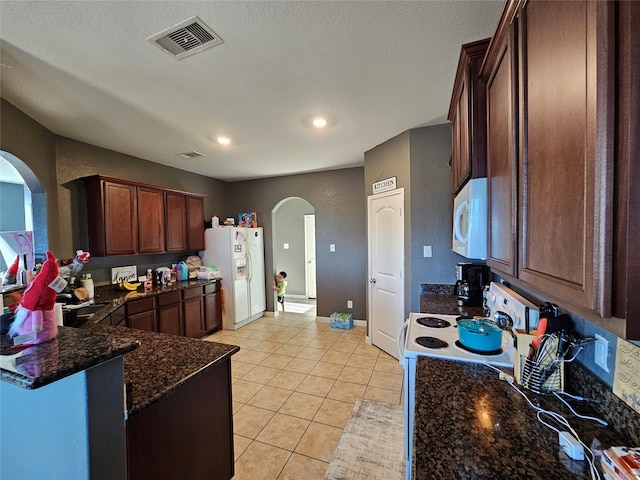 kitchen with light tile patterned flooring, white appliances, dark stone counters, and a textured ceiling