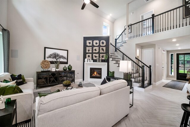 living room with a ceiling fan, a towering ceiling, stairs, baseboards, and a glass covered fireplace