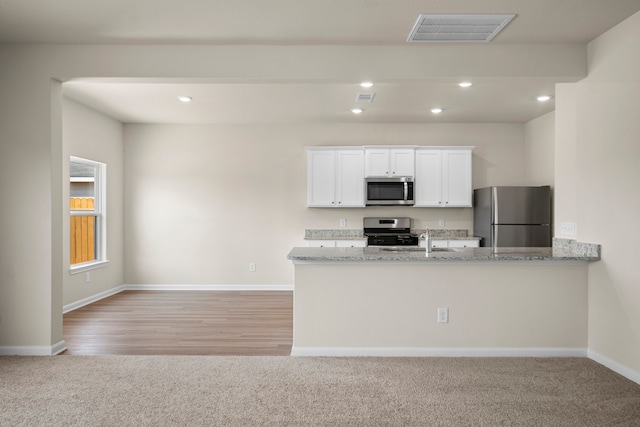 kitchen with light stone counters, stainless steel appliances, kitchen peninsula, and white cabinets