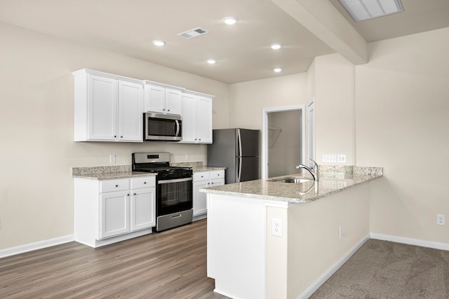 kitchen featuring appliances with stainless steel finishes, sink, white cabinets, light stone counters, and kitchen peninsula