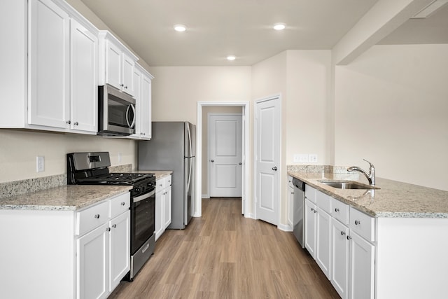 kitchen featuring sink, white cabinetry, stainless steel appliances, light stone counters, and light wood-type flooring