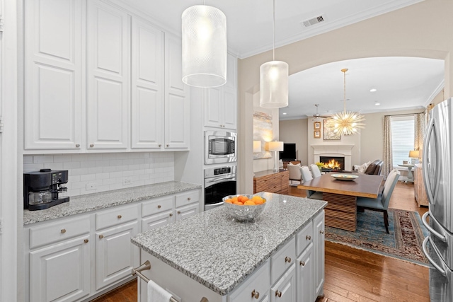 kitchen featuring pendant lighting, stainless steel appliances, a center island, ornamental molding, and white cabinets