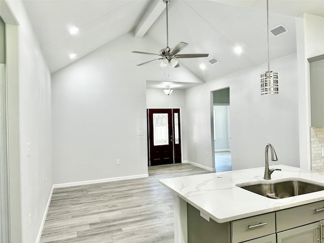 kitchen featuring pendant lighting, beamed ceiling, sink, light stone counters, and light hardwood / wood-style floors