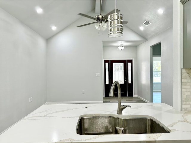 kitchen with sink, ceiling fan, vaulted ceiling with beams, light stone countertops, and decorative light fixtures