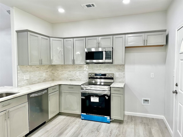 kitchen featuring gray cabinets, appliances with stainless steel finishes, light stone counters, and light hardwood / wood-style floors