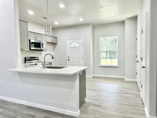 kitchen with gray cabinets, appliances with stainless steel finishes, decorative light fixtures, sink, and light hardwood / wood-style flooring