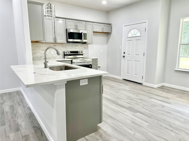 kitchen featuring pendant lighting, gray cabinets, backsplash, stainless steel appliances, and kitchen peninsula