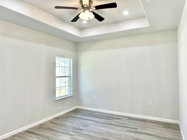 empty room with a raised ceiling, ceiling fan, and light wood-type flooring