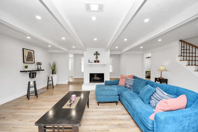 living room with beamed ceiling, a fireplace, and light hardwood / wood-style floors