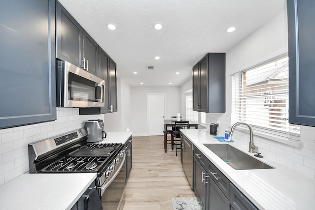 kitchen with stainless steel appliances, sink, light hardwood / wood-style floors, and decorative backsplash