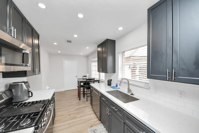 kitchen featuring appliances with stainless steel finishes, sink, backsplash, a textured ceiling, and light hardwood / wood-style flooring