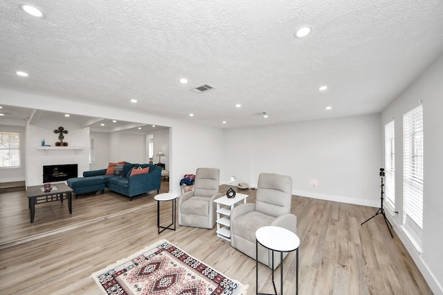 living room featuring a large fireplace, a wealth of natural light, a textured ceiling, and light hardwood / wood-style floors