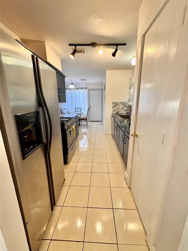 kitchen featuring tasteful backsplash, light tile patterned floors, track lighting, stainless steel fridge, and black gas stove