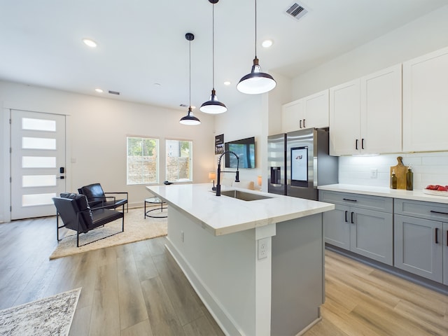 kitchen with gray cabinets, stainless steel refrigerator, decorative light fixtures, an island with sink, and sink