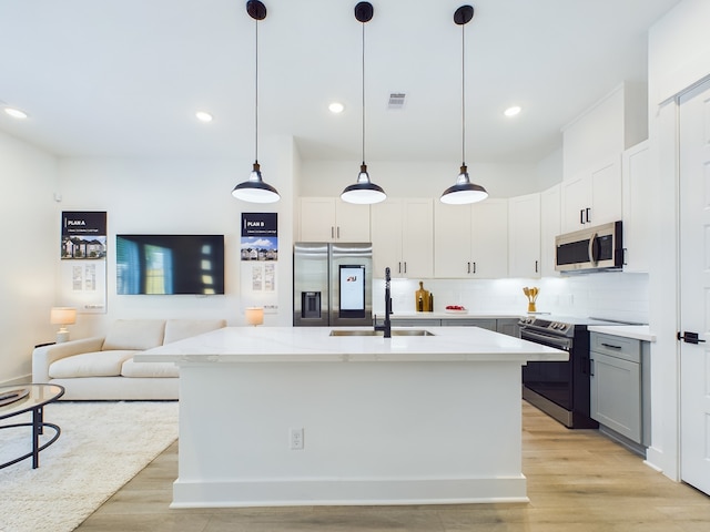 kitchen featuring sink, pendant lighting, stainless steel appliances, a kitchen island with sink, and white cabinets