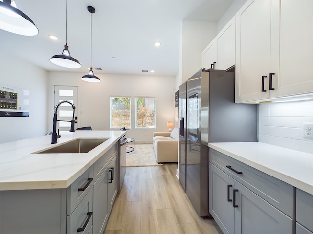 kitchen with light stone counters, sink, pendant lighting, and gray cabinetry