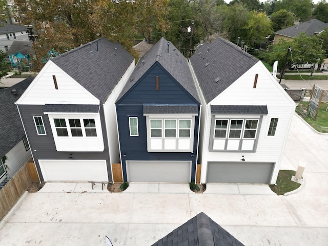 rear view of property featuring an attached garage, roof with shingles, fence, and driveway