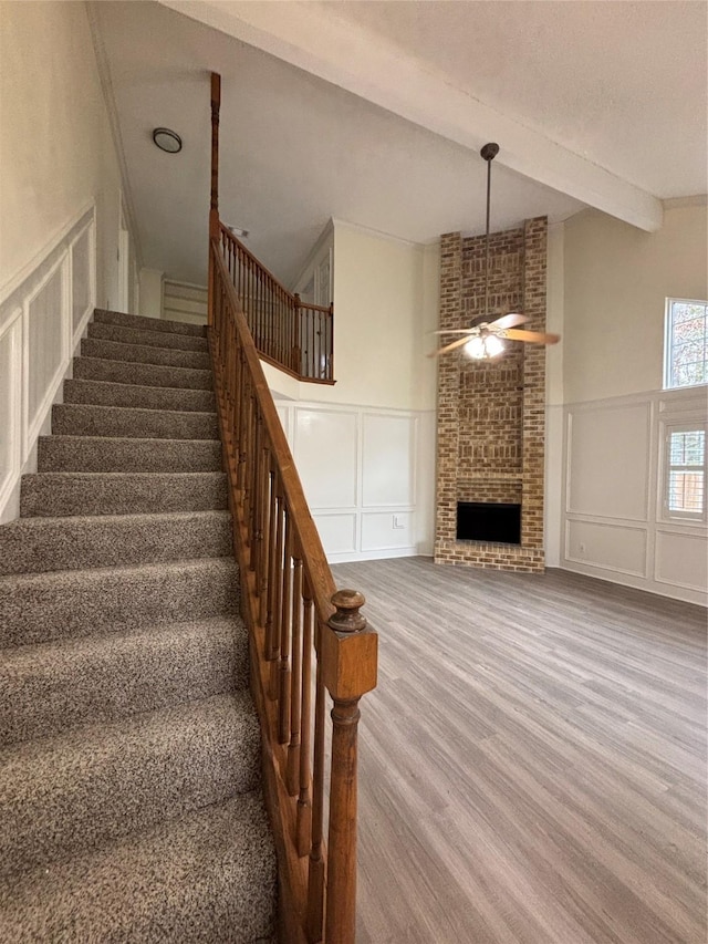 stairs with a textured ceiling, beamed ceiling, ceiling fan, a fireplace, and hardwood / wood-style floors