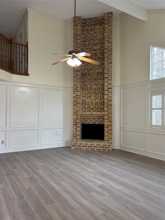 unfurnished living room with crown molding, a brick fireplace, light wood-type flooring, and beam ceiling