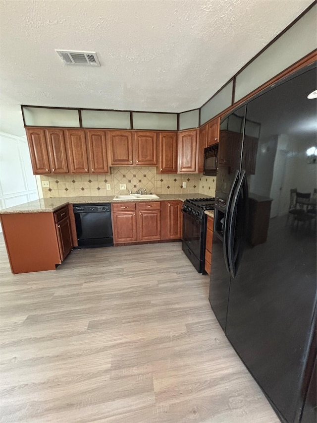 kitchen featuring sink, black appliances, a textured ceiling, light hardwood / wood-style floors, and backsplash