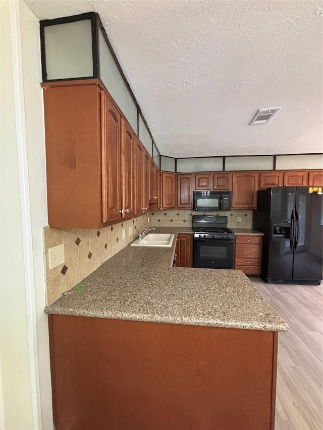 kitchen with sink, tasteful backsplash, black appliances, light hardwood / wood-style floors, and kitchen peninsula