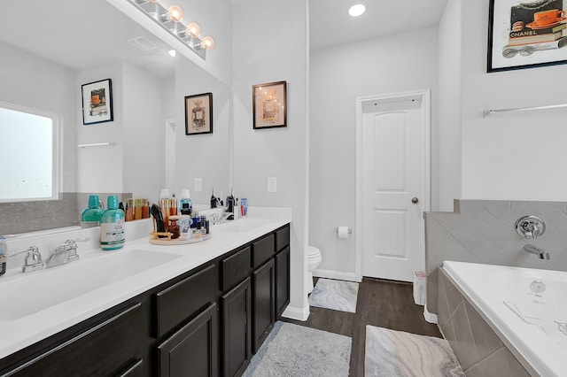 bathroom featuring vanity, wood-type flooring, tiled bath, and toilet