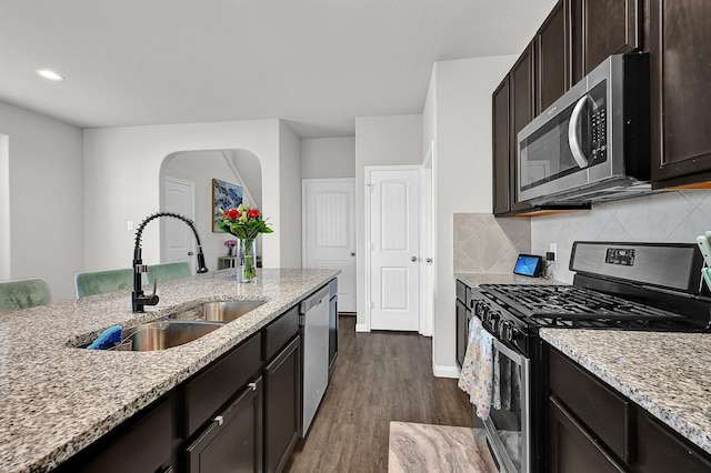 kitchen with sink, dark brown cabinets, dark hardwood / wood-style floors, stainless steel appliances, and light stone countertops