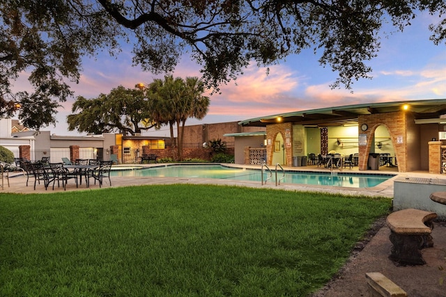 pool at dusk featuring a lawn and a patio area