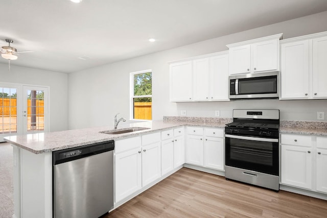 kitchen with appliances with stainless steel finishes, sink, white cabinets, light hardwood / wood-style floors, and kitchen peninsula