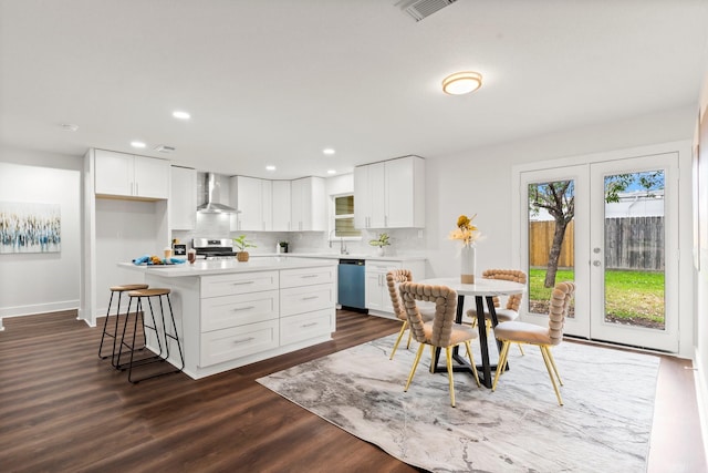 kitchen with stainless steel appliances, a kitchen island, wall chimney range hood, and white cabinets