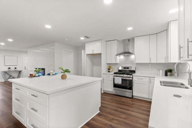 kitchen featuring a kitchen island, white cabinetry, sink, stainless steel gas range, and wall chimney exhaust hood